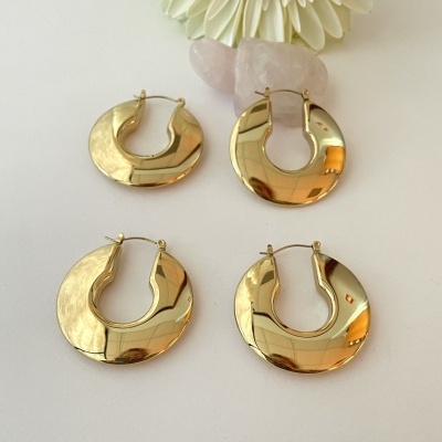 Dois pares de brincos de argola dourada com superfície lisa sobre superfície branca com flor e pedras rosa