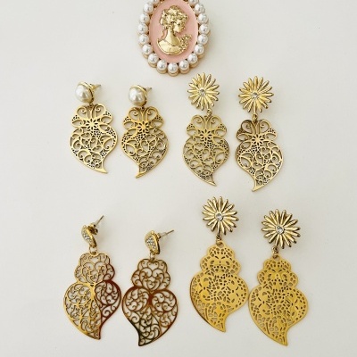 Brincos dourados decorativos e broche oval rosa com pérolas num fundo branco