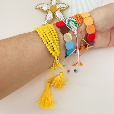 Pulseiras artesanais multicoloridas no pulso com flor decorativa ao fundo