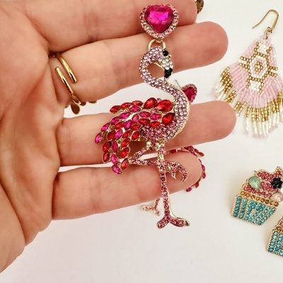 Brinco flamingo com pedras vermelhas e rosa sendo segurado pela mão