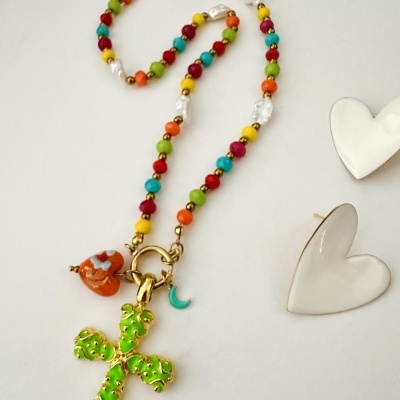 Colar colorido com pendentes de cruz verde, coração laranja e lua azul num fundo branco com brincos coração.