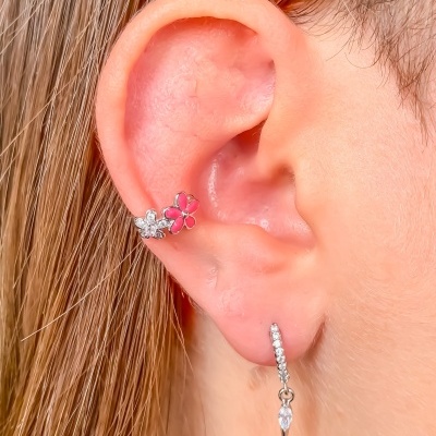 Orelha com brincos prateados, um de argola com pendente e outro de pressão com flores pequenas vermelha e branca.