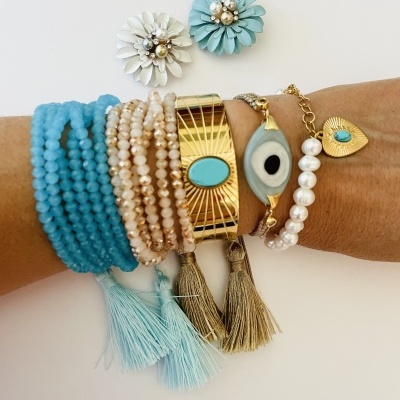 Pulseiras e brincos azuis, dourados e pérola numa mão com fundo branco