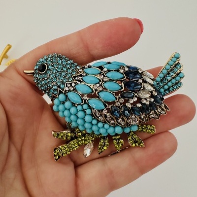 Broche pássaro azuis e verdes com detalhes dourados na mão