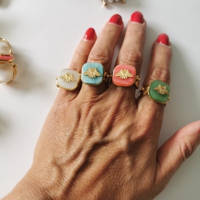 Mão com quatro anéis quadrados coloridos com abelhas douradas