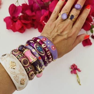 Mão com anéis e pulseiras coloridos sobre fundo com flores vermelhas.