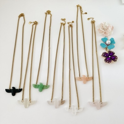 Colares com pendentes de pássaros e broches florais coloridos sobre superfície branca