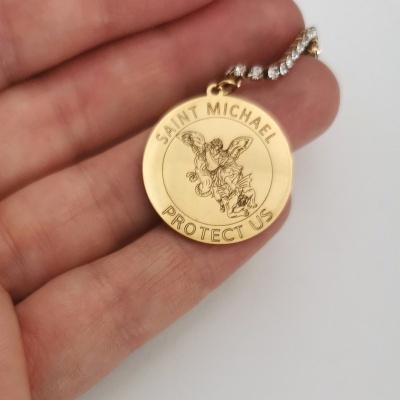 Medalha dourada redonda com gravura de São Miguel e texto. Pendura numa corrente com brilhantes.