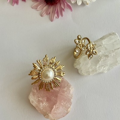 Brincos dourados com pérola e detalhes de folhas sobre pedras e flores coloridas