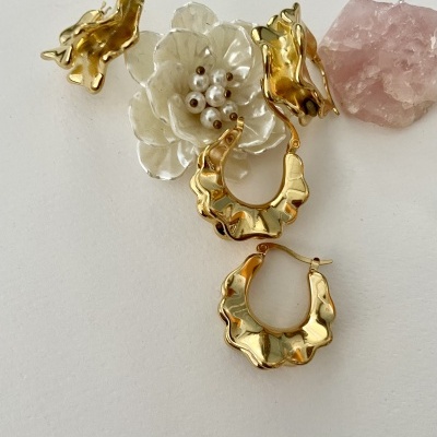 Brincos dourados ondulados e flor branca com pérolas junto a pedra rosa
