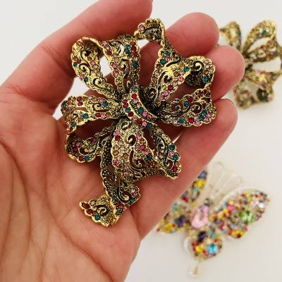 Broche dourado em forma de laço com pedras coloridas na mão