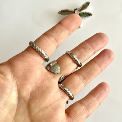 Mão com cinco anéis prateados de diferentes designs.