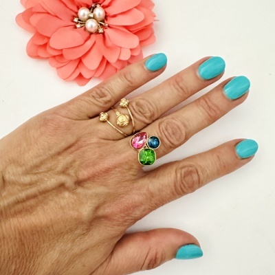 Mão com unhas azuis e anéis dourados coloridos perto de flor cor de rosa.