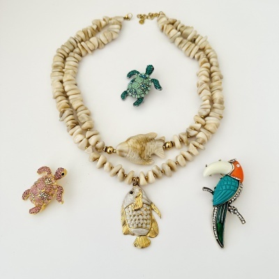 Colar de contas bege com pendentes de peixe e tartaruga e três broches coloridos em fundo branco