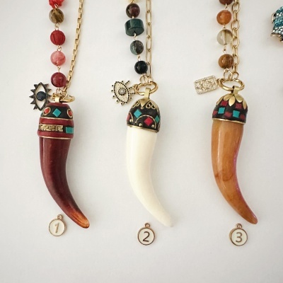 Três colares com pendentes em forma de corno decorados com padrões geométricos e pingentes metálicos