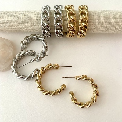 Anéis e brincos de argola retorcida em tons prateado e dourado sobre fundo claro
