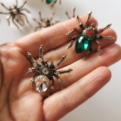 Brincos aranha com pedras verdes e transparentes em mão, fundo branco