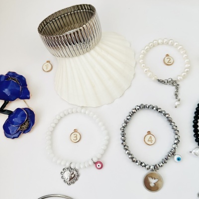 Quatro pulseiras com diferentes materiais e designs numeradas de 1 a 4 sobre fundo branco, com concha e flor azul ao lado.