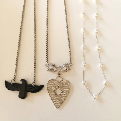 Três colares: pássaro preto, coração prateado com estrelas, corrente prateada com pérolas