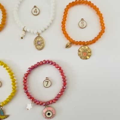 Três pulseiras coloridas com contas e pendentes e etiquetas com números em fundo branco