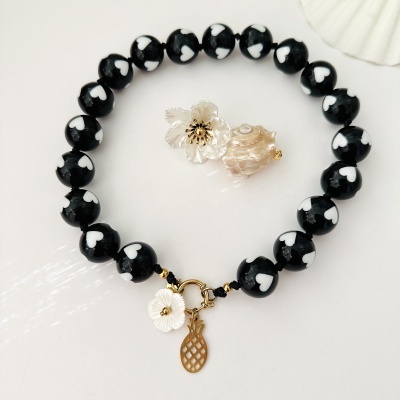 Pulseira com contas negras com corações brancos e fecho dourado com pendente de abacaxi e flor branca