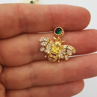 Brinco de abelha dourado com pedras transparentes e verde.