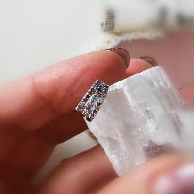 Brinco pequeno com pedras coloridas segurado sobre um cristal branco