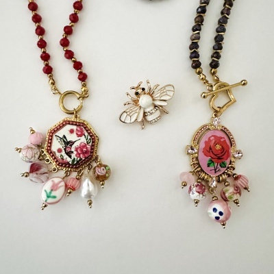 Colares e broche decorativos com contas vermelhas, rosas e douradas e pendentes florais.