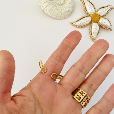Mão com anéis dourados e broches decorativos em concha e flor