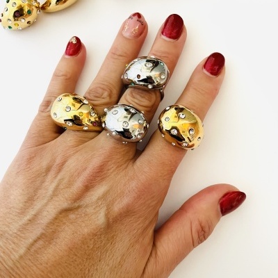 Mão com anéis grandes dourados e prateados com cristais coloridos