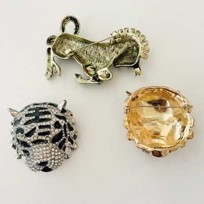 Três broches de metal em formas de cavalo e tigre sobre fundo branco