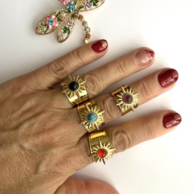 Mão com quatro anéis dourados com pedras coloridas e broche de libélula dourado decorado