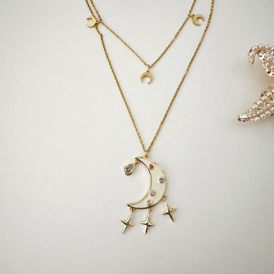 Colar dourado com pingentes de lua e estrelas em fundo branco