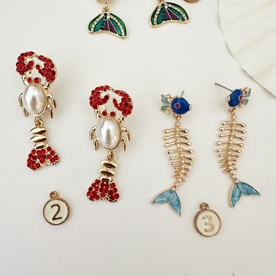 Brincos temáticos de lagosta vermelha e peixe esqueleto azul em fundo branco.