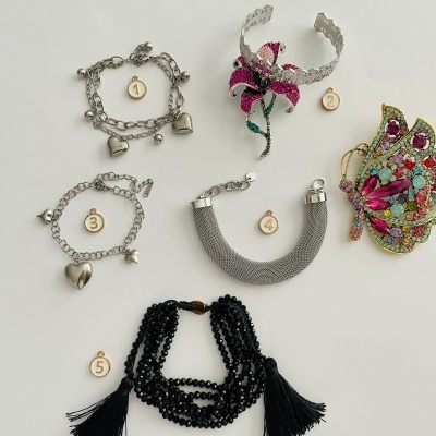 Bijuteria variada incluindo pulseiras prateadas, bracelete com flor rosa, colar preto de contas e aplicação de borboleta colorida