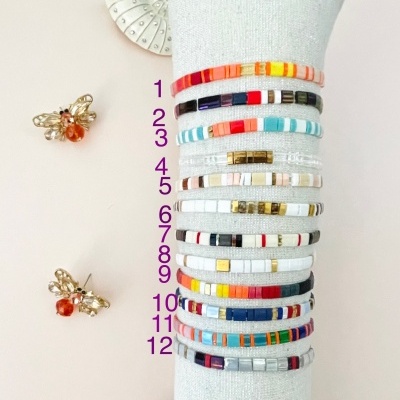 Conjunto de pulseiras coloridas sobre almofada branca com acessórios de abelha ao lado