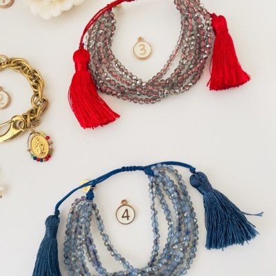 Pulseiras de contas cinza com cordão e tassel vermelho e azul sobre fundo branco.