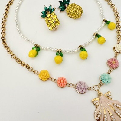 Brincos de ananás com pedras amarelas e verdes, colar de pérolas com limões amarelos, e colar dourado com flores em resina e pendente em forma de concha
