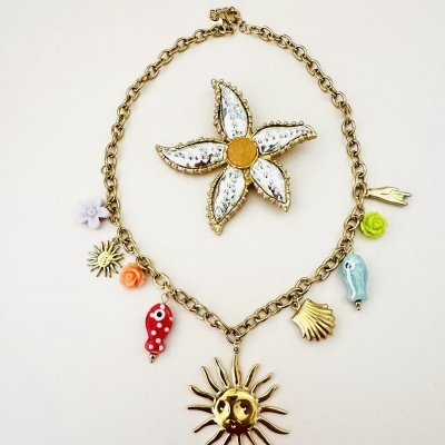 Colar dourado com pendentes coloridos e flor decorativa ao fundo