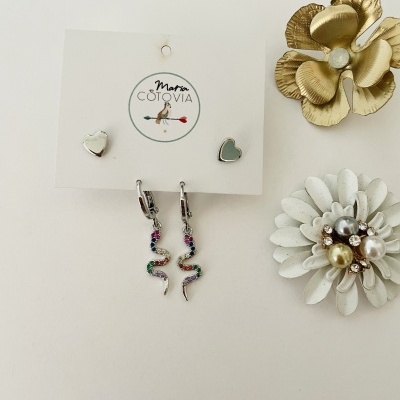 Brincos Maria Cotovia com formato de coração e cobra, acessórios florais decorativos dourado e branco próximos.