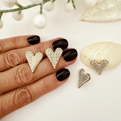 Brincos de coração dourados com pedras em fundo branco com decoração