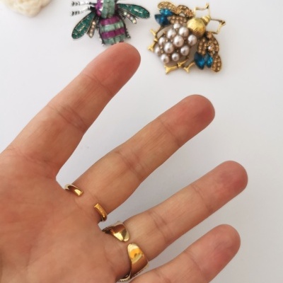 Mão com anéis dourados e broches de abelha coloridas sobre fundo branco