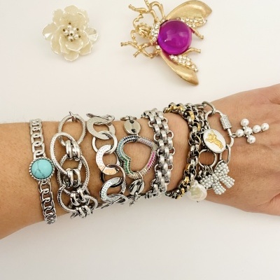 Pulseiras metálicas variadas no braço e dois broches decorativos em fundo branco