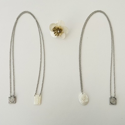 Quatro colares com pendentes metálicos em fundo branco com flor decorativa