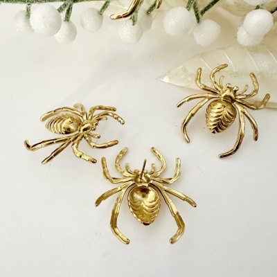 Brincos dourados em forma de aranha com decoração branca ao fundo