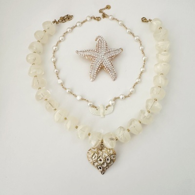Colares e broche em fundo branco com pendentes e pedras, incluindo estrela do mar.