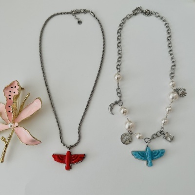 Três colares com pendentes de borboleta e pérolas em fundo branco