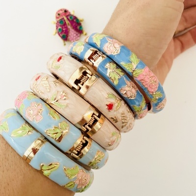 Pulseiras esmaltadas florais azul claro e bege com fechos dourados num pulso