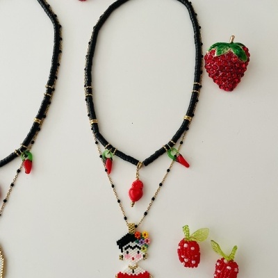 Colar com contas pretas, douradas e pingentes vermelhos, figura de mulher pixelada e frutas feitas de contas