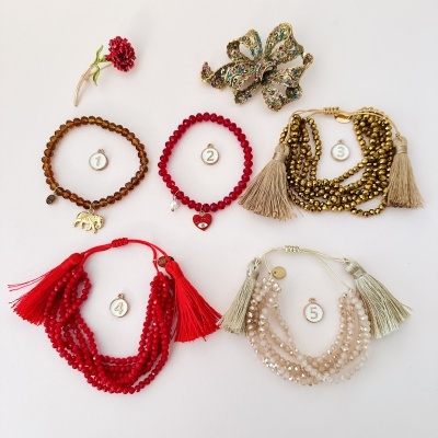 Cinco conjuntos de bijuterias numerados sobre fundo branco com laço decorativo multicolorido